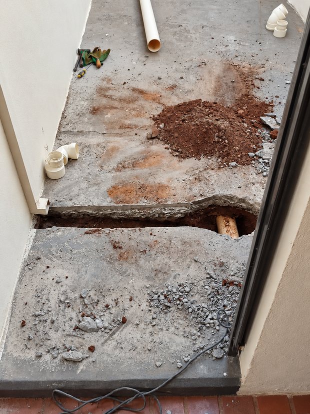 Corredor com o contrapiso quebrado e a tubulação de esgoto exposta
