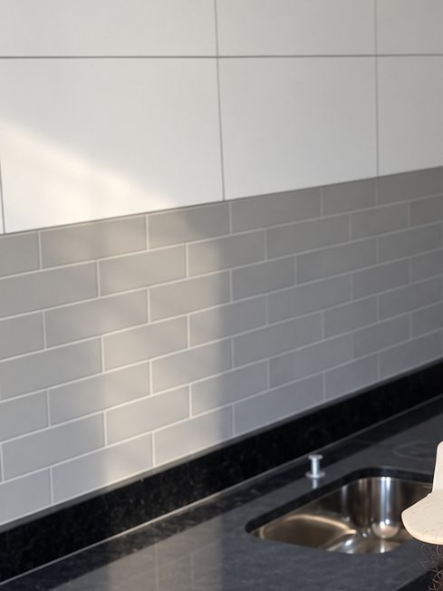 Cozinha com bancada de granito preto, cuba de inox e revestimento branco e cinza