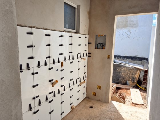 Parede de banheiro com revestimento branco sendo assentado com espaçadores niveladores